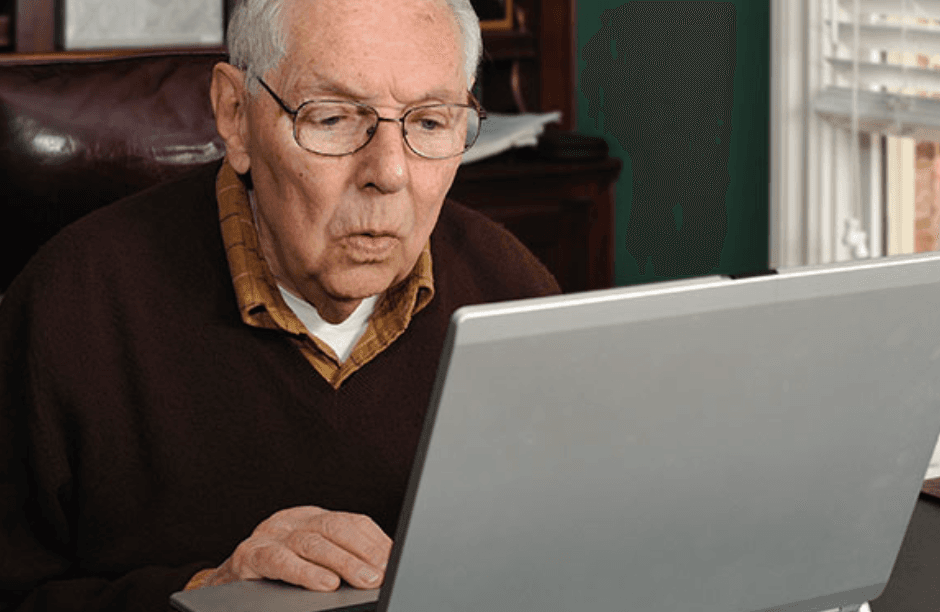 An older man leaning close to his laptop screen, reading a message with a concerned expression