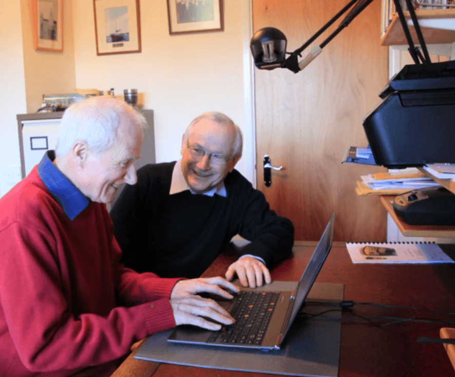 Two older men working through something on a laptop together at a home desk